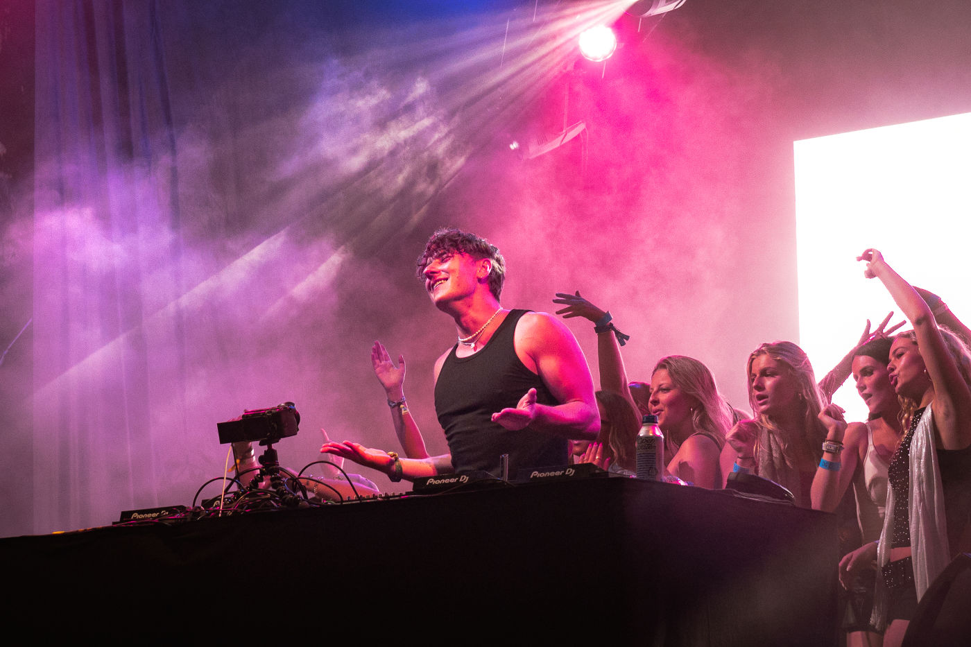 a dj on stage under pink lights, crowd in silhouette