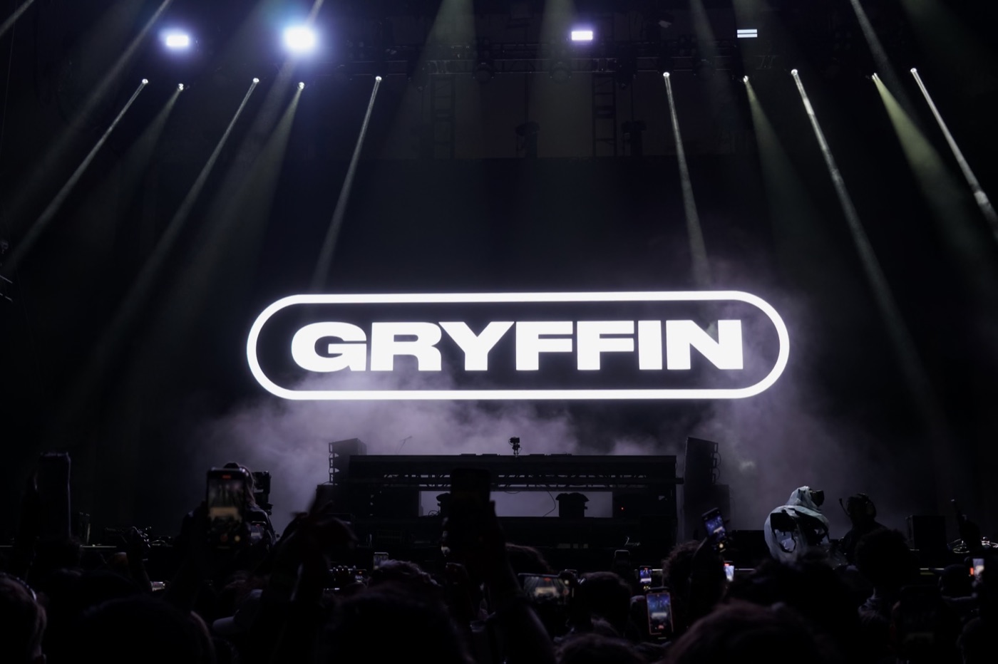 a glowing gryffin logo over a hazy stage, phones raised in the crowd