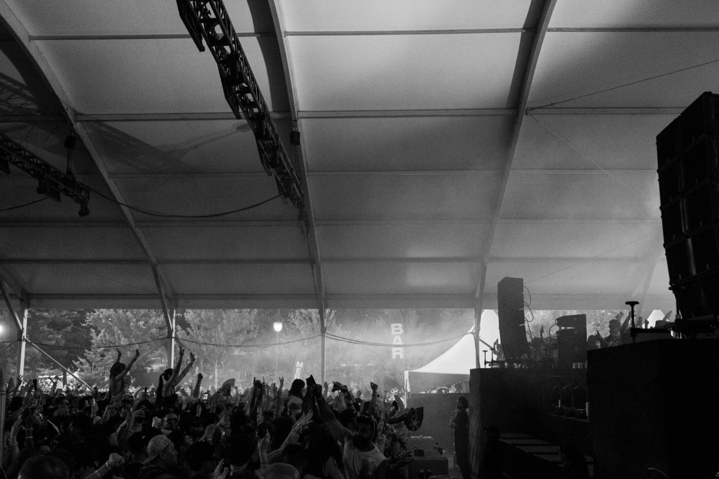 a packed crowd with hands up under a festival tent, in black and white