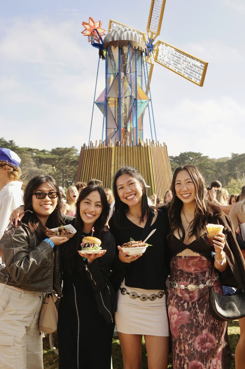 four friends holding festival food in front of a giant windmill sculpture