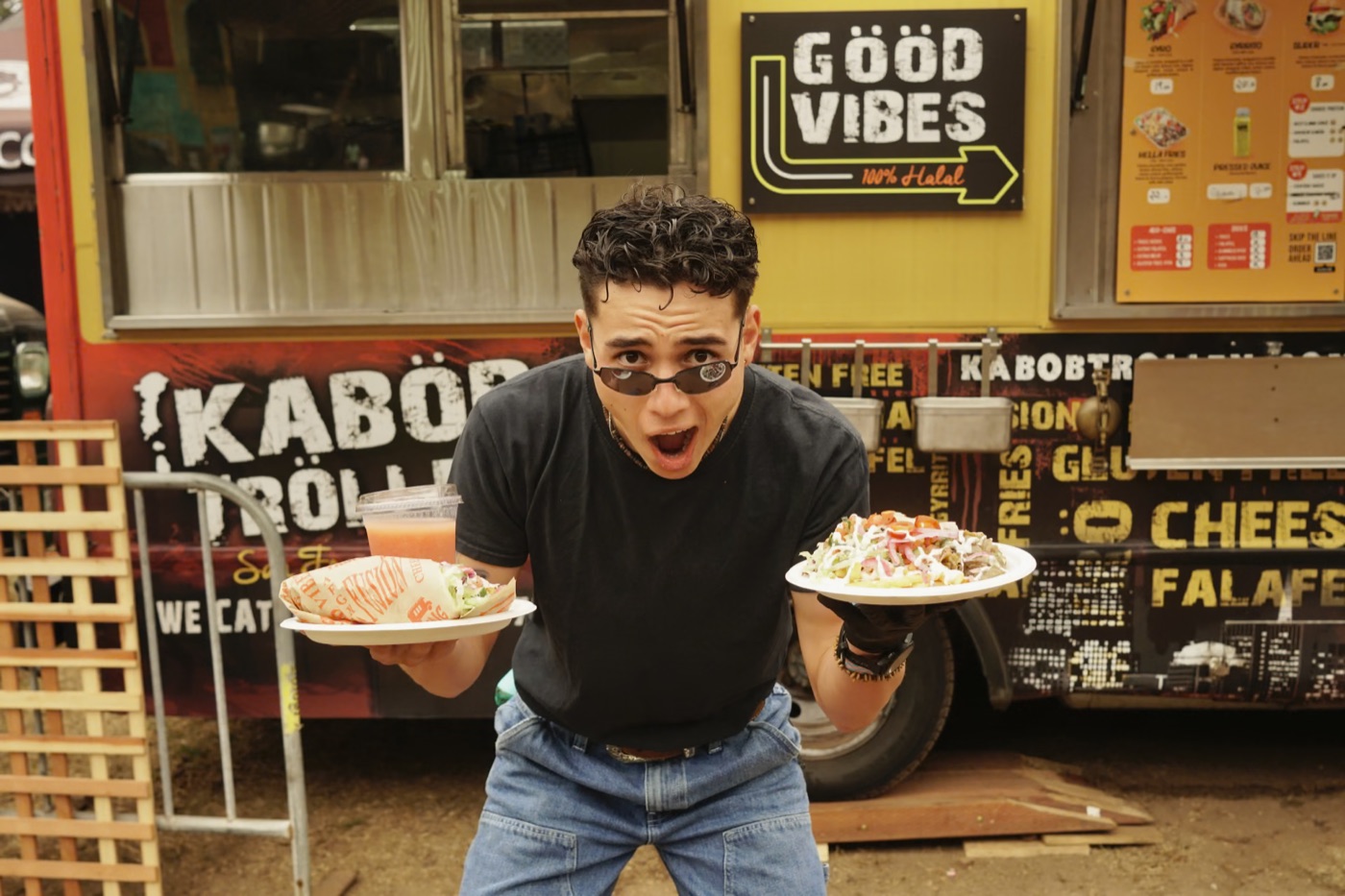 a guy in tiny sunglasses holding two plates in front of a halal food truck