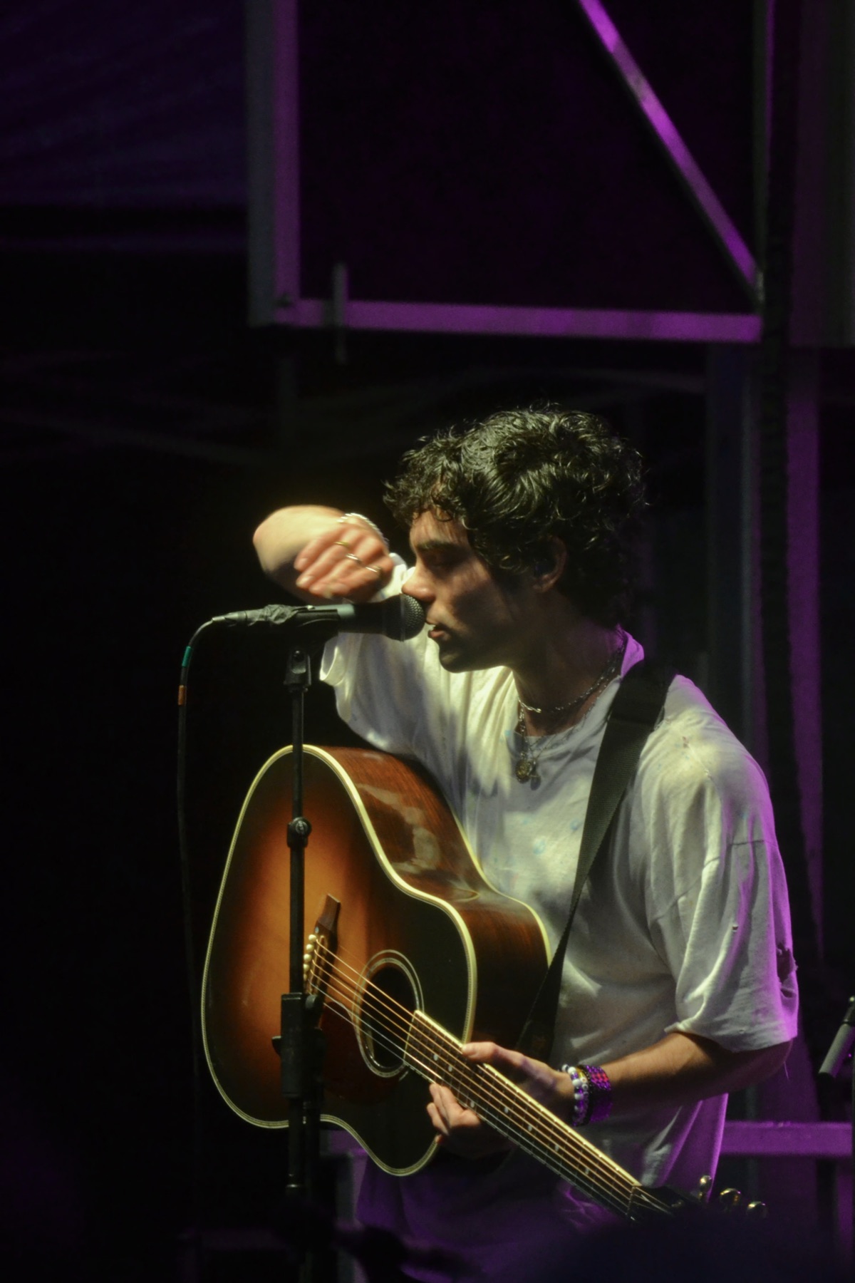 a singer with an acoustic guitar leaning into the mic under purple light